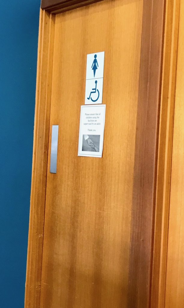 a big and heavy wooden toilet door, with labels showing an image of a woman, and a wheelchair