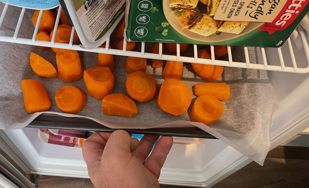 a freezer door is open, and a baking tray, has baking paper on it, and the pieces of carrot - freezing carrots cooking