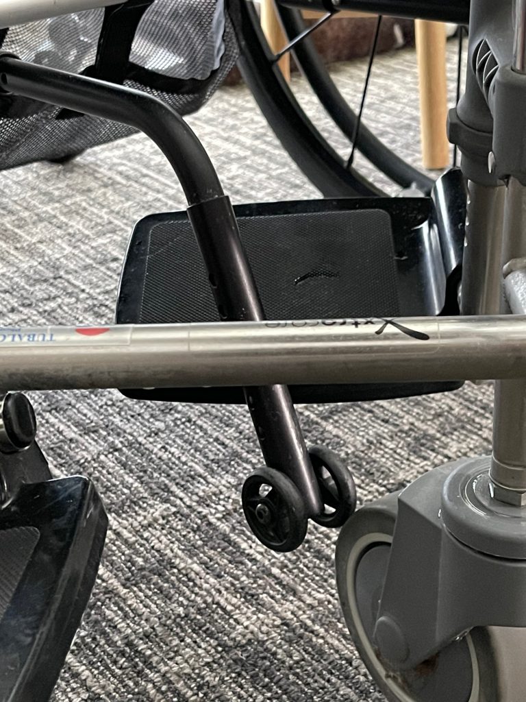 The shower chair foot rest hooks onto the anti-tip mechanism of the manual chair