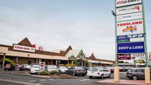 a large sign showing a few of the shops in the centre, a car park behind it with about 30 cars in it, and further back is the shopping centre - Sefton Plaza Accessibility